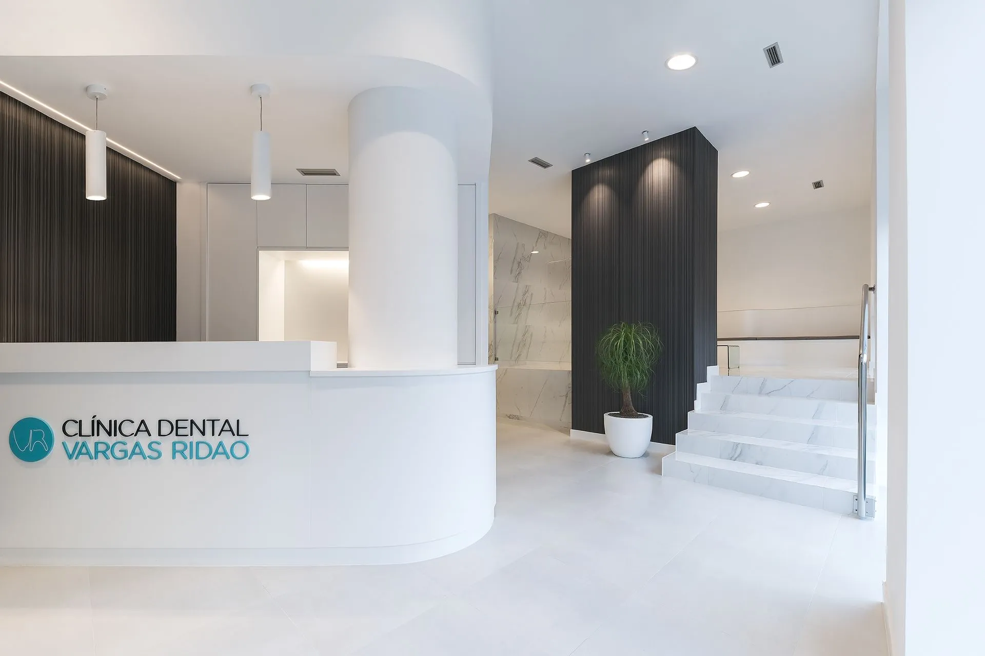 Recepción de la Clínica Vargas Ridao en Vigo, con el logotipo sobre el mostrador y escalera de mármol